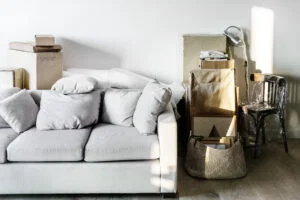 A light grey sofa and old furniture join packed boxes in a sunlit room, ready for moving.