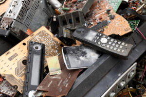 A pile of old, broken electronics—including circuit boards, a cracked phone, and a damaged cordless phone—awaits removal during your next garage cleanout.